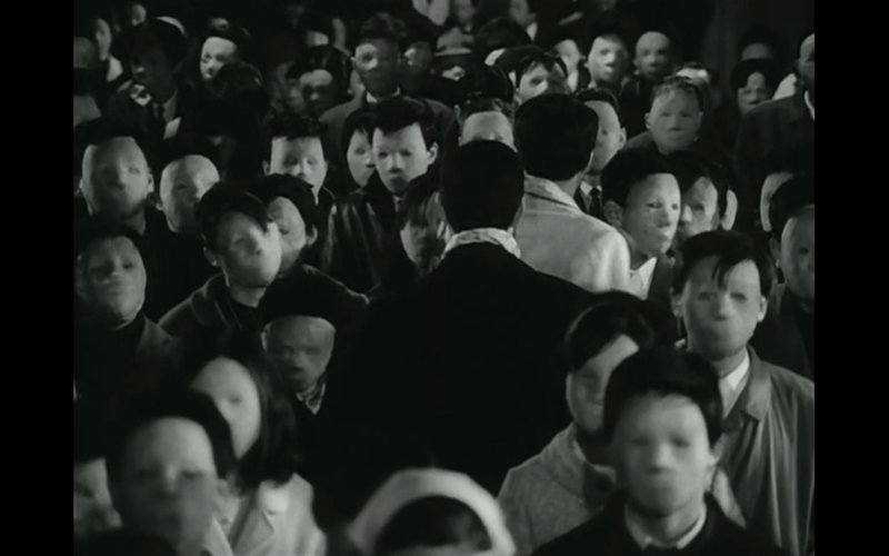 a shot of a man in a black coat, standing among crowd with blurry creepy faces 